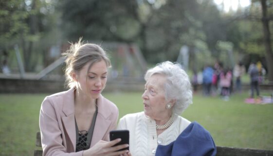 adult daughter teaching senior mother using smartphone in park