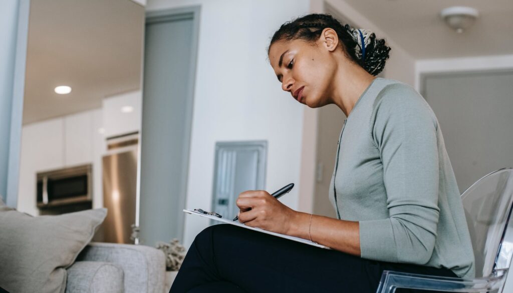 concentrated ethnic female interviewer or psychotherapist taking notes in clipboard